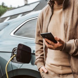 Man charging electric car, checking progress in app.